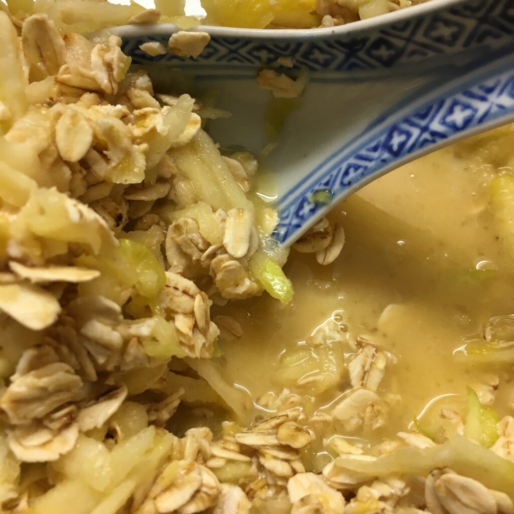 in a bowl there are rolled oats combined with orange juice and grated apple ready to soak over night